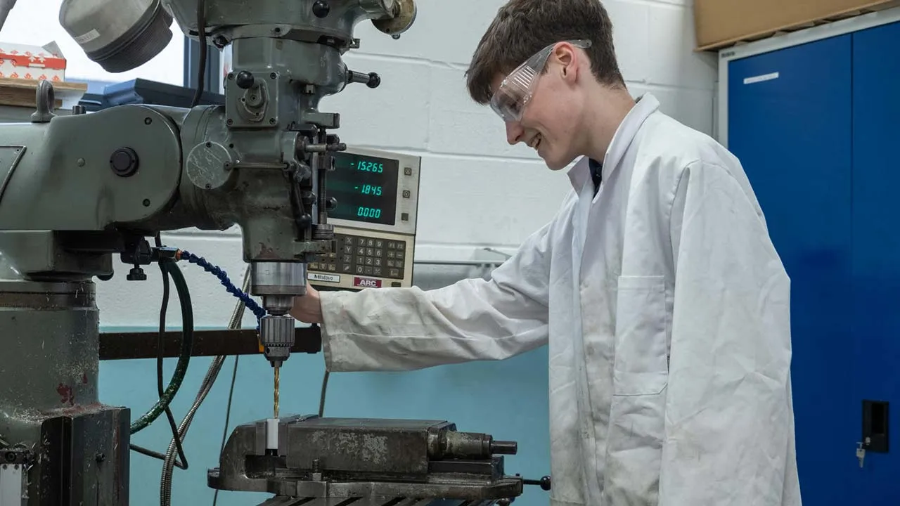 A student in a lab coat focuses on adjusting a complex machine in a laboratory setting