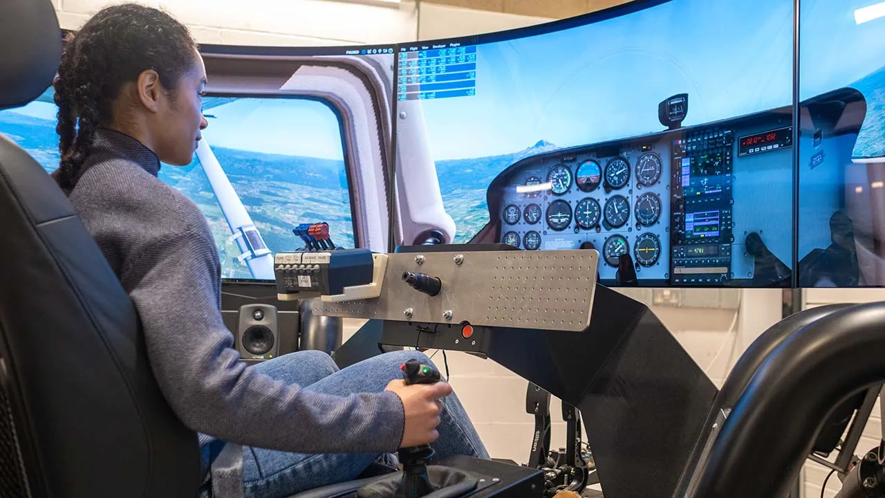 A student using a flight simulator with controls and large screens in front of them