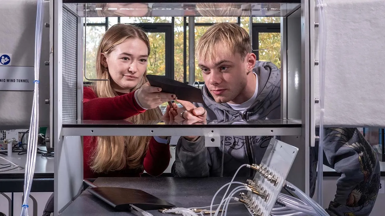 Two students standing side by side looking at a item that is in a machine