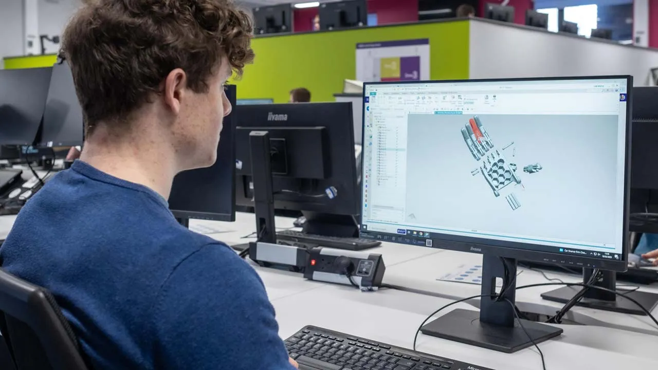 A student sitting at a desk looking at a technical drawing on a computer screen