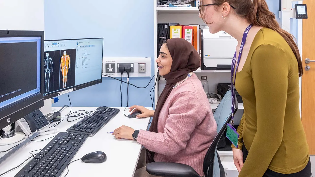 Two people are looking at a computer that has scans of a human body showing on the screen