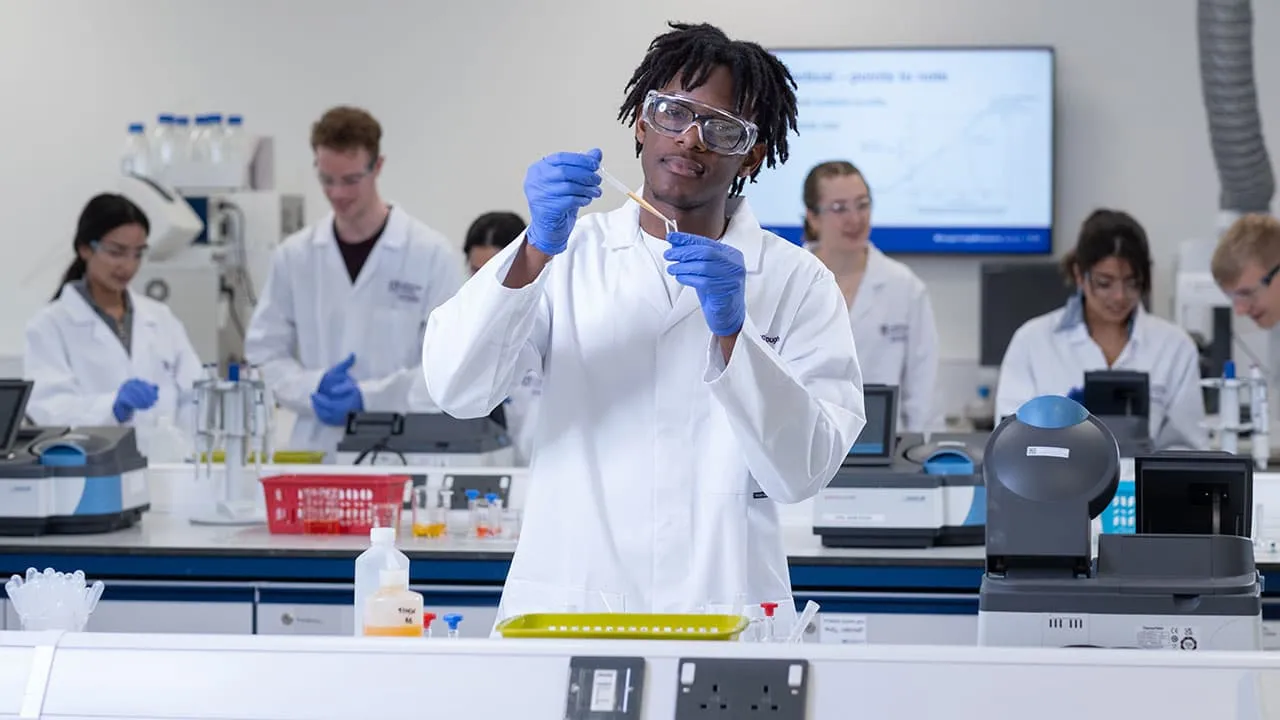 A chemistry student in a lab coat and gloves is engaged in research, examining materials on a lab bench