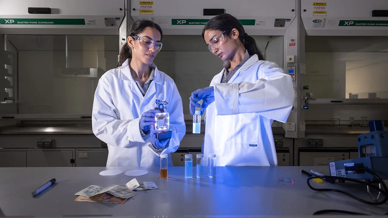 Two students in lab coats carrying out a chemistry experiment with test tubes and surrounded by lab equipment