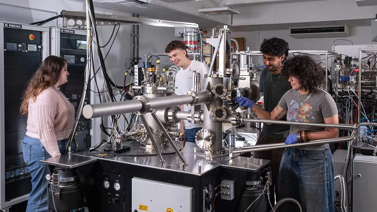 Four students work together at a machine, immersed in their scientific research and experiments