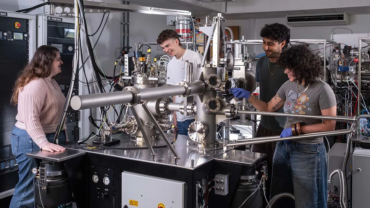 Four students work together at a machine, immersed in their scientific research and experiments