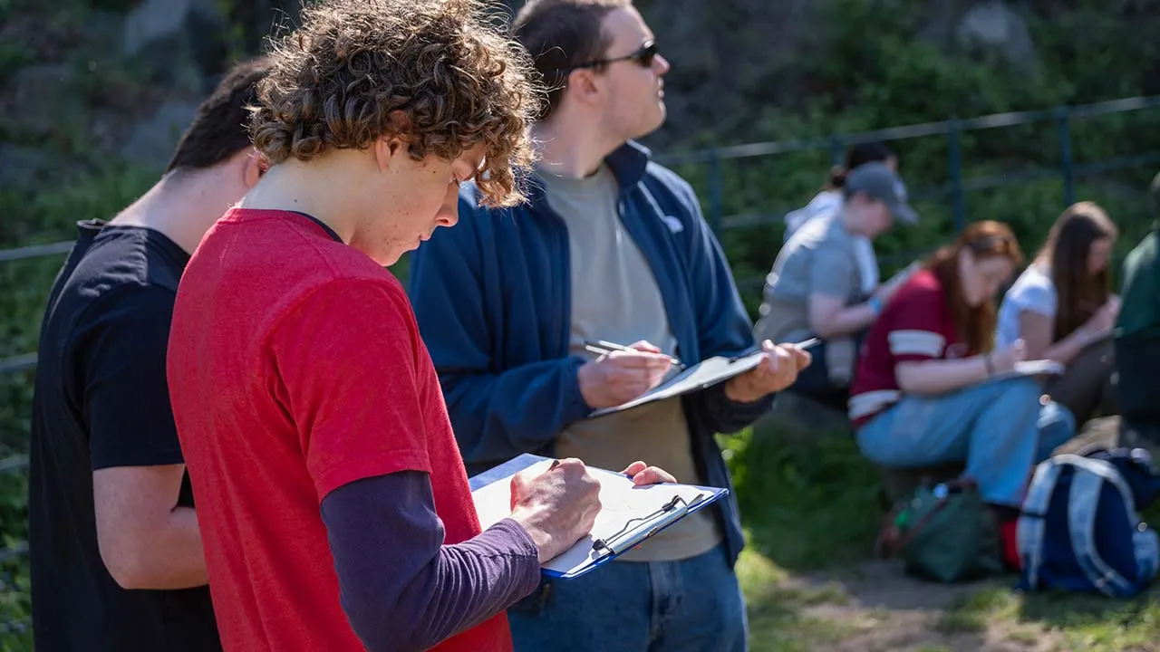 A group of geography students in the field writing on clipboards