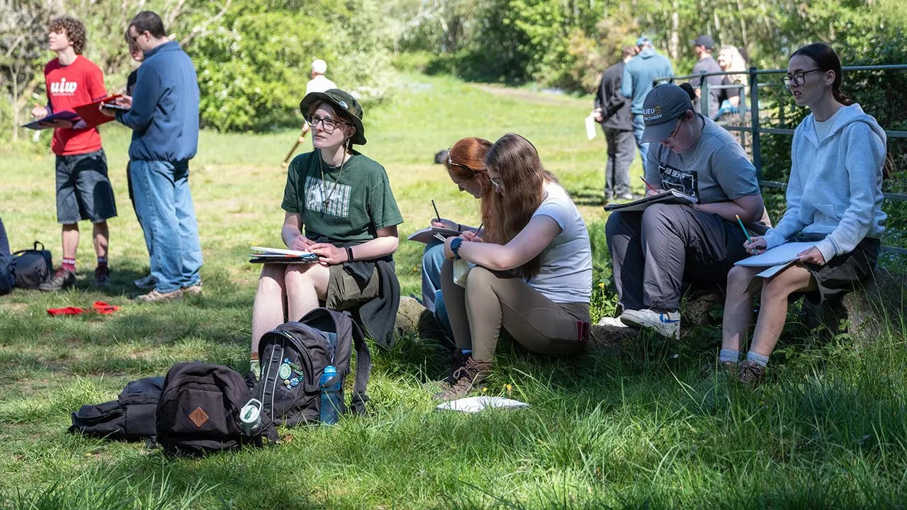 A group of students sitting outside on a geography field trip, taking notes.