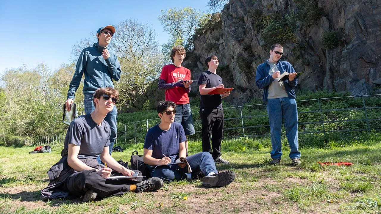 A group of geography students outdoors on a field trip. They are holding clipboards and taking notes