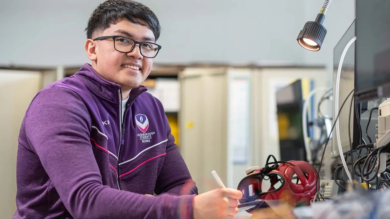 A student wearing a purple ɫ������ Sport top is sat at a desk writing.