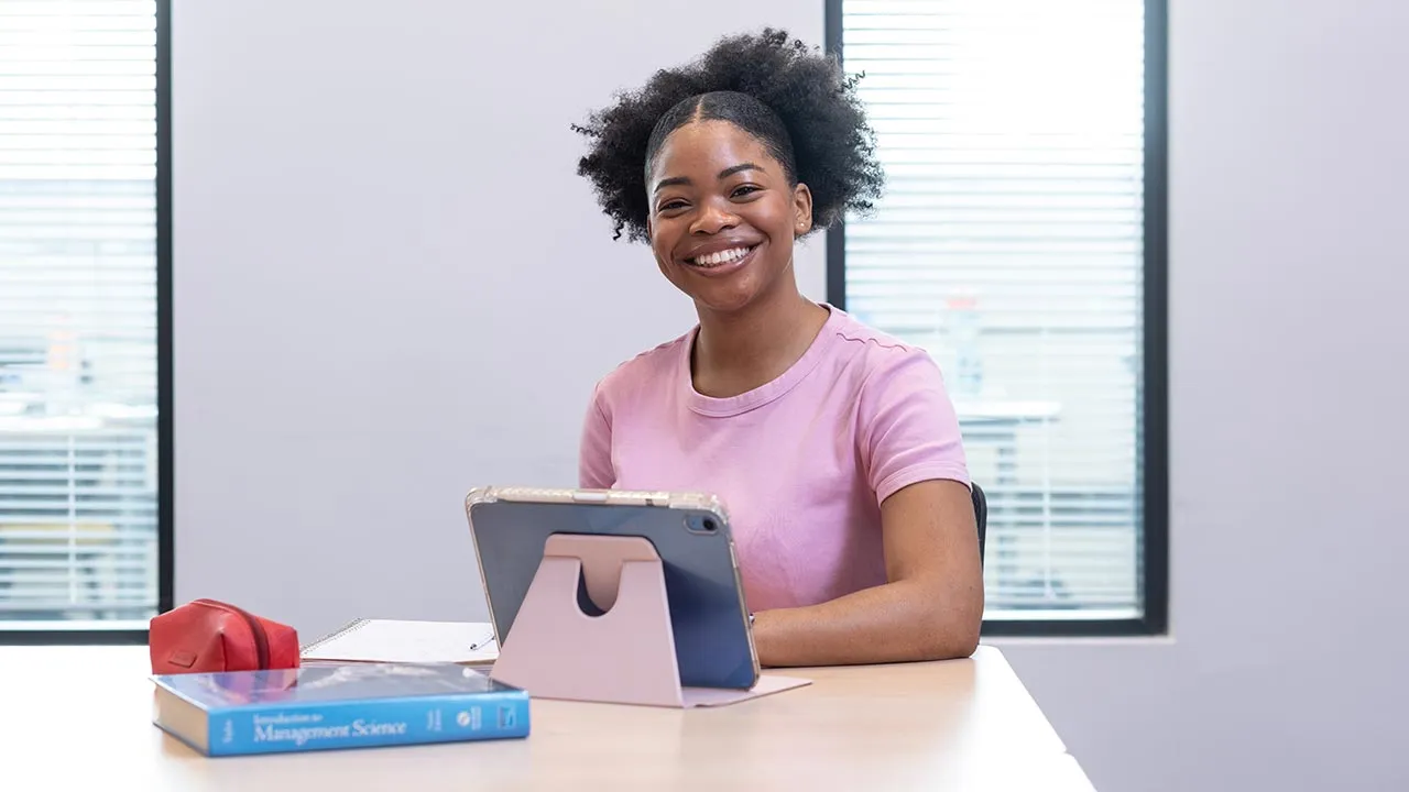 A woman sat at a desk with a tablet device and international management book in front of her