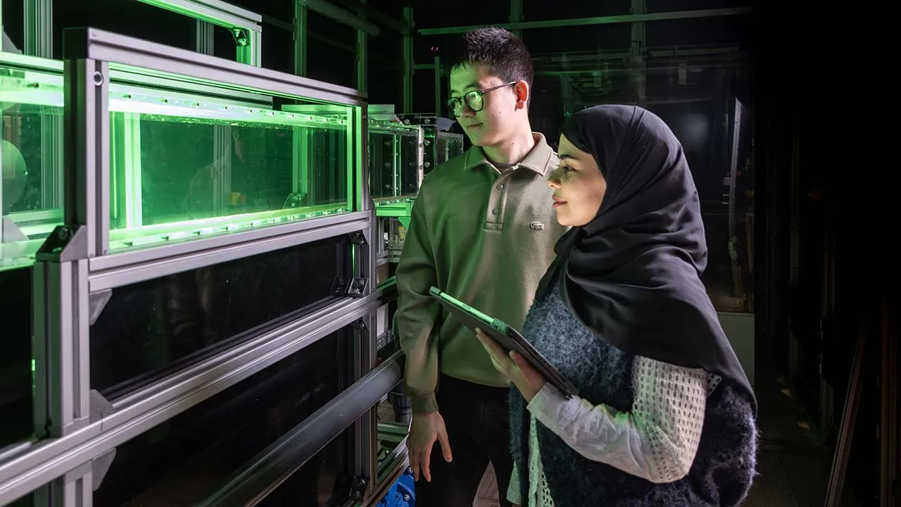 Two students working on their research in a lab, one student is holding a tablet device.
