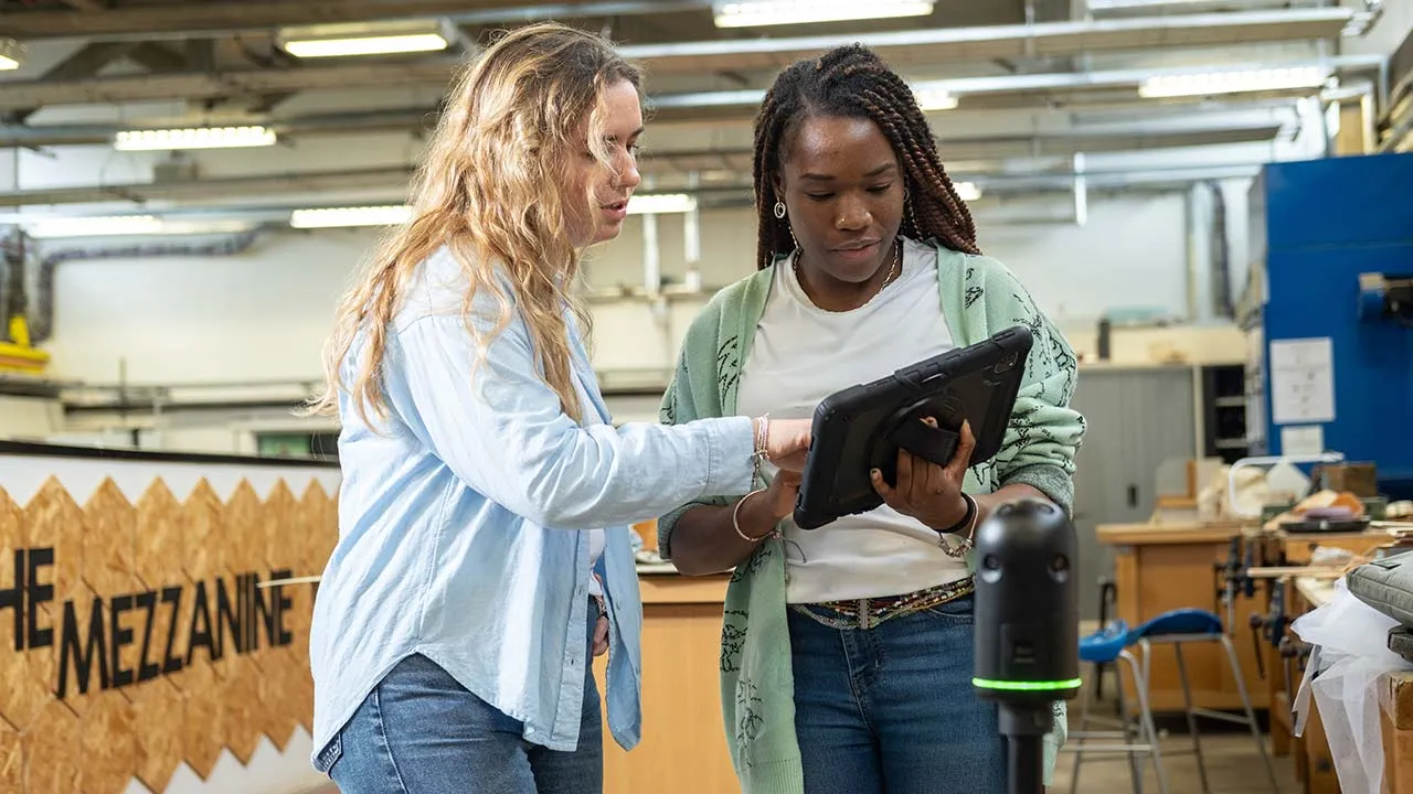 Two students focus on a tablet device in a workshop