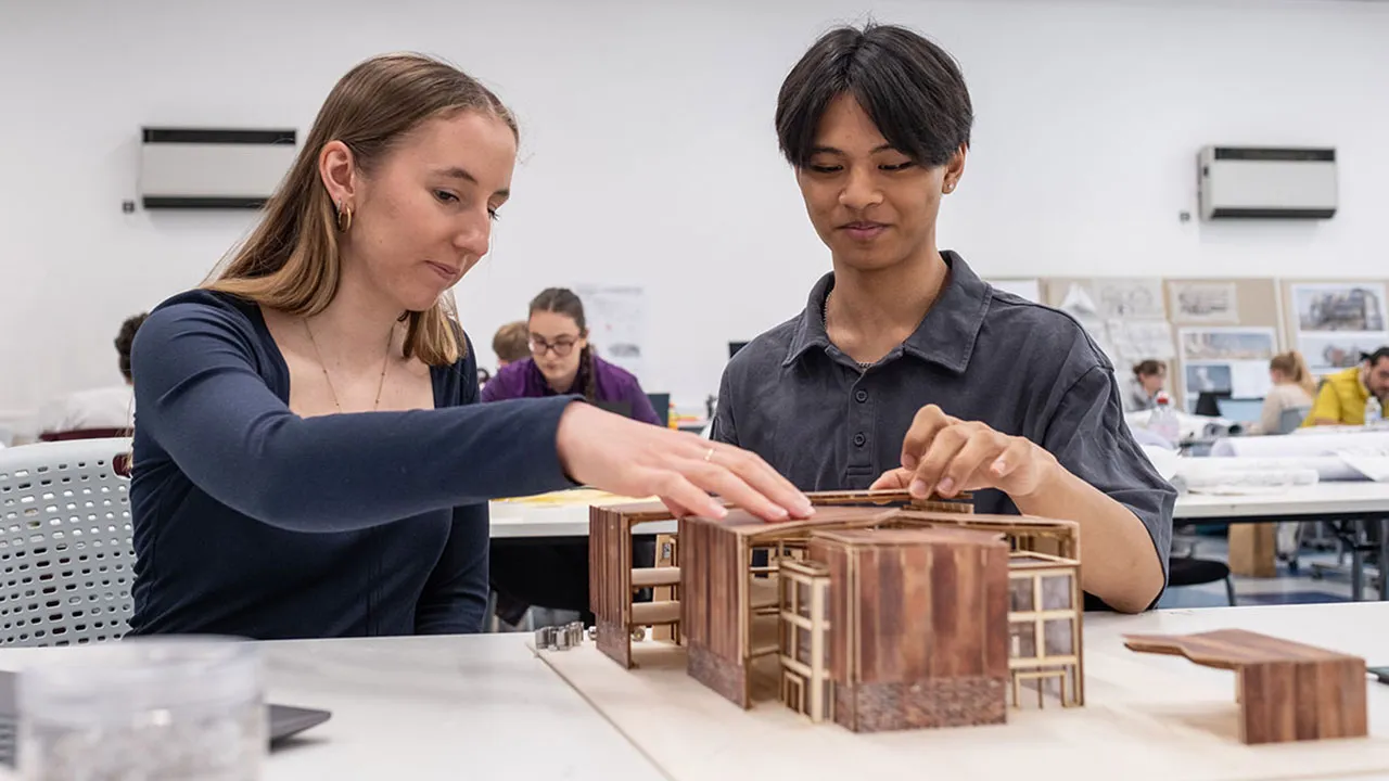 Two students work side by side on a detailed building model
