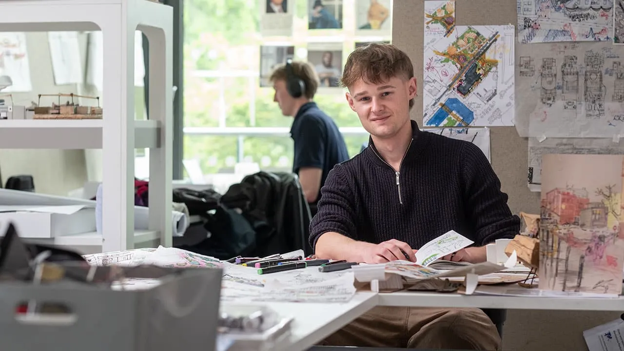 A student working at a desk surrounded by architectural drawings