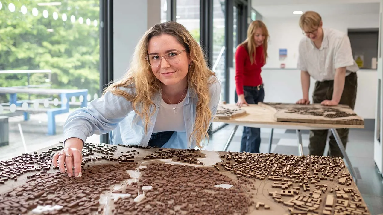 Three students looking at town models displayed on table tops
