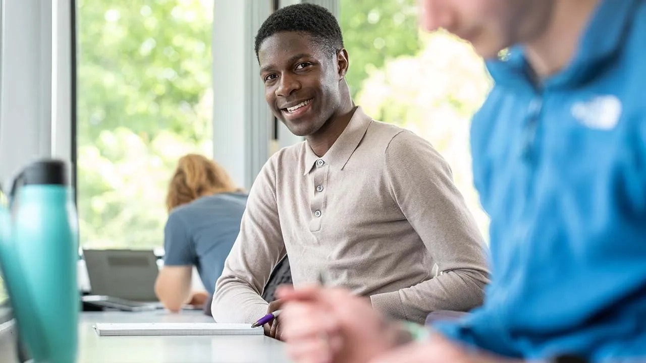 A student is sat at a table holding a pen with a notebook in front of them