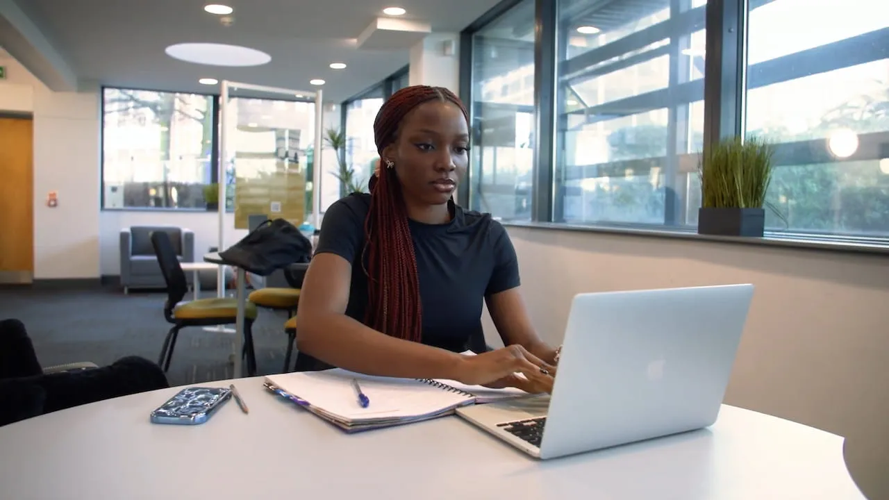 A female student sitting in an open space working on a laptop