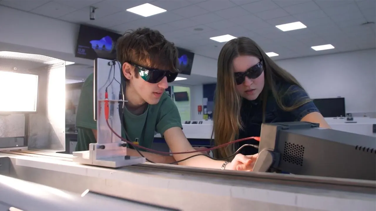 Two students wearing protective eye glasses are carrying out an electrical experiment in a lab