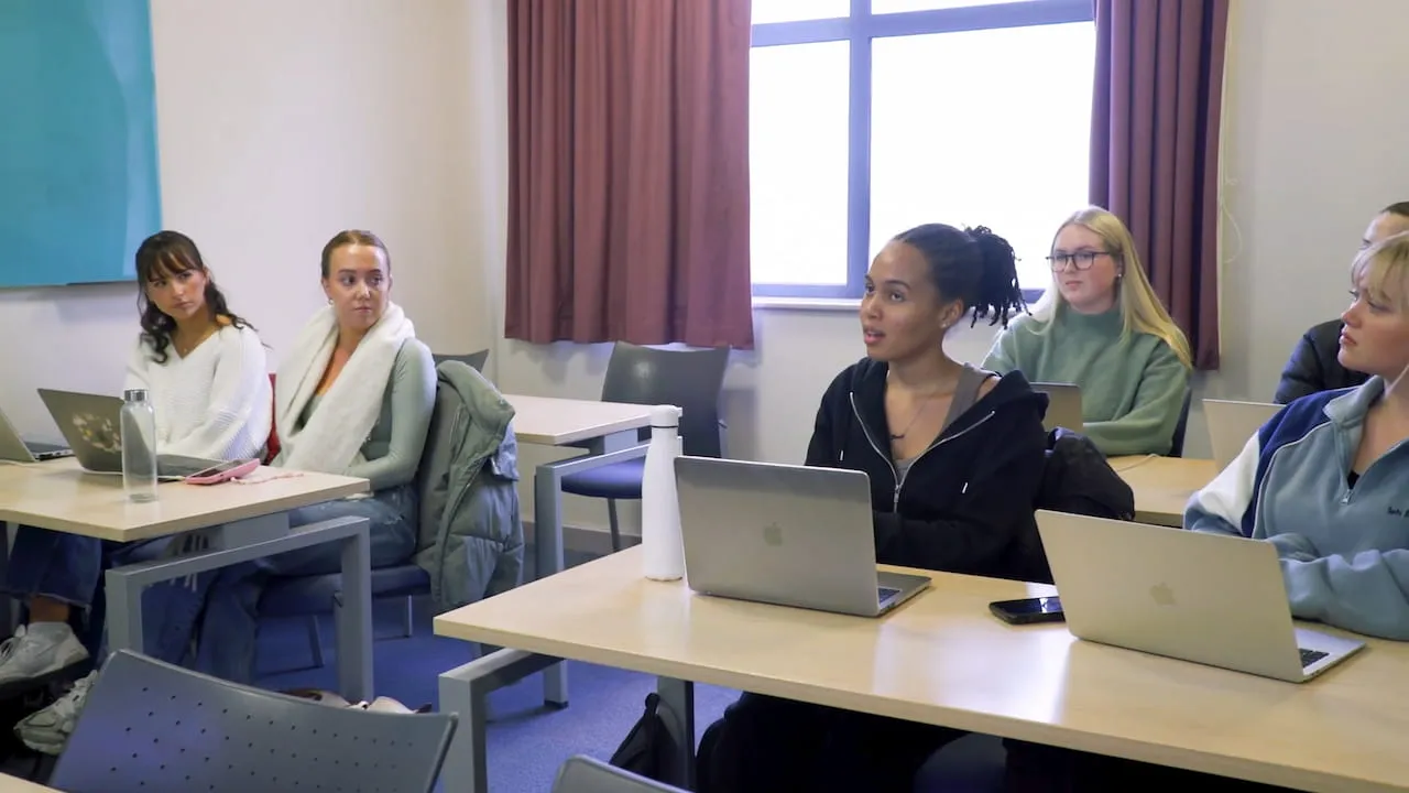 A group of students sitting at desks with laptops open taking part in a seminar
