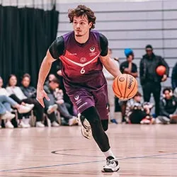 Justin Hedley on a basketball court dribbling the ball with spectators watching in the background