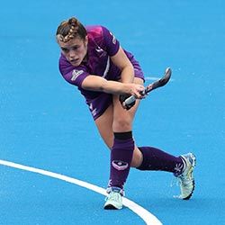 Lorna Mackenzie on a blue hockey pitch holding a hockey stick