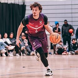 Justin Hedley on a basketball court dribbling the ball with spectators watching in the background