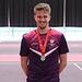 George Houghton wearing a medal whilst stood on a pink and purple tennis court