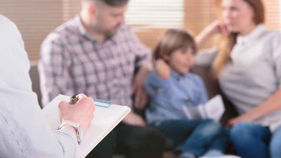 child sat with parents and another adult with clipboard and paper