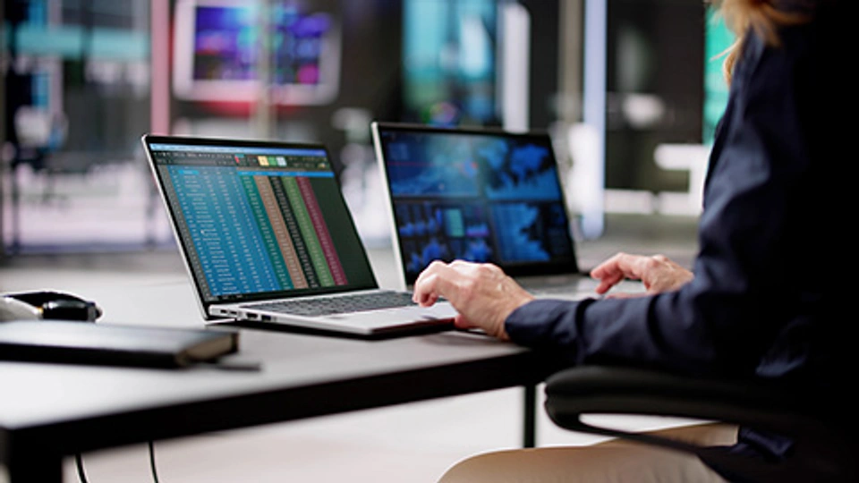 Person using two laptops displaying data and analytics dashboards in a digital workspace