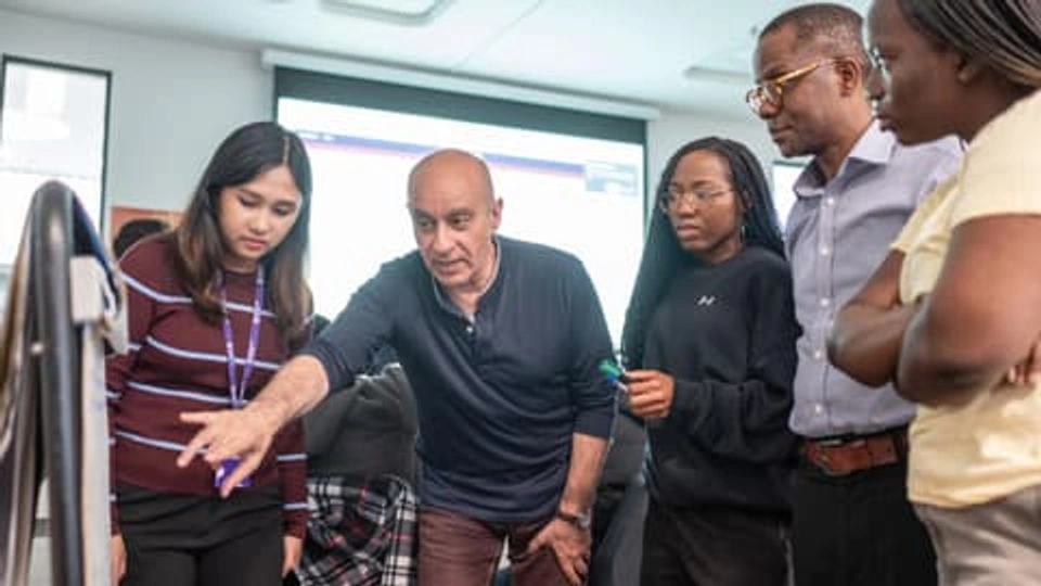 An academic demonstrates something on a flip chart to a gathering of four students.