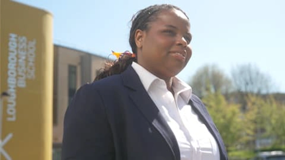 A female MBA student in a white shirt and blue jacket walking away from the Business School building.