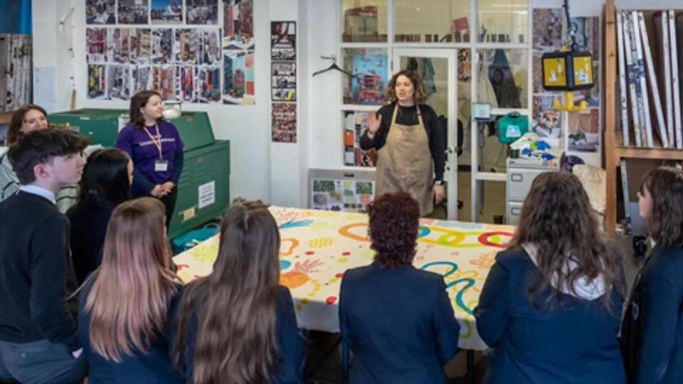 Teacher stands around a table talking to students sitting down
