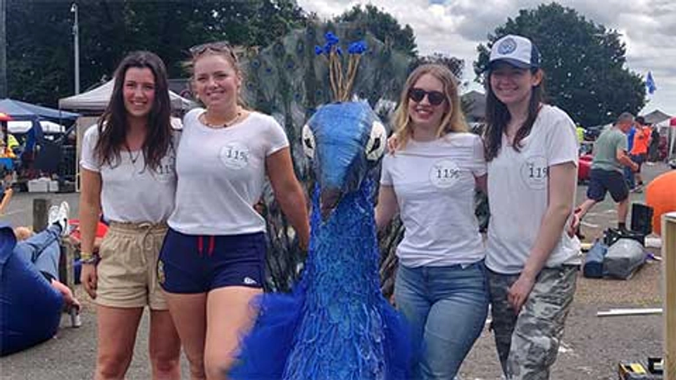 Four students are standing in a line, with two on either side of a red-bull soapbox peacock-style racing cart. 