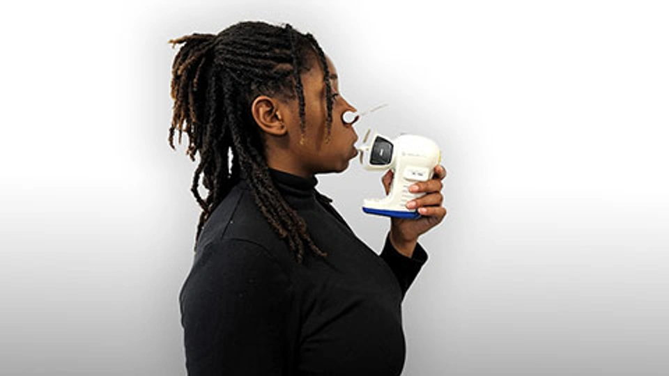 A woman holding a breath analyser to her mouth