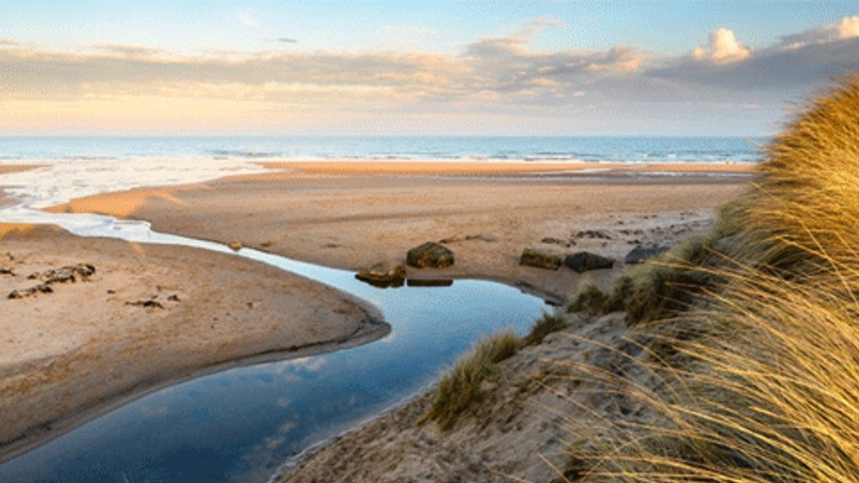 a beach in the UK with a coastal stream and cloudy sky