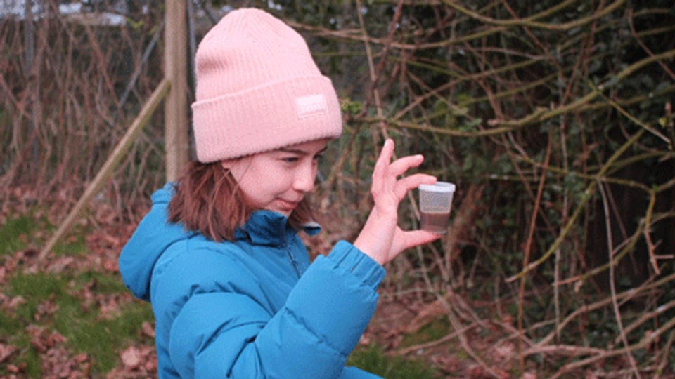 a girl standing outside holding a cup of soil