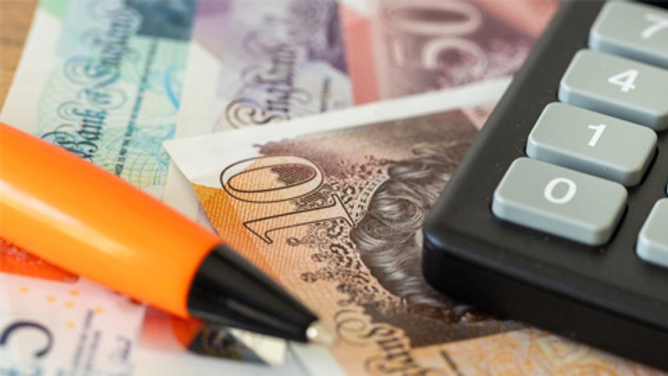 a pen and calculator on top of ten pound notes
