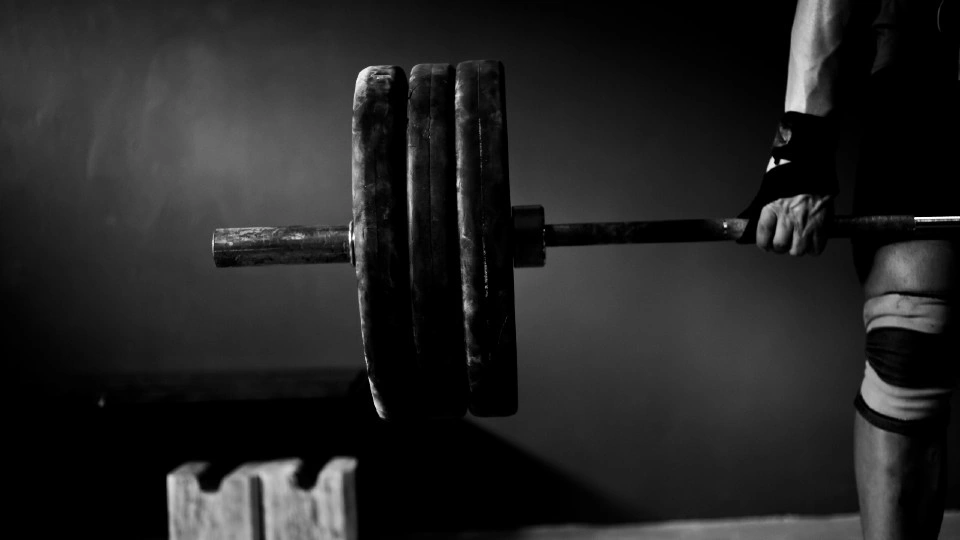 A black and white photo showing the end of a barbell with three weighted plates on it, being lifted in the air by a person