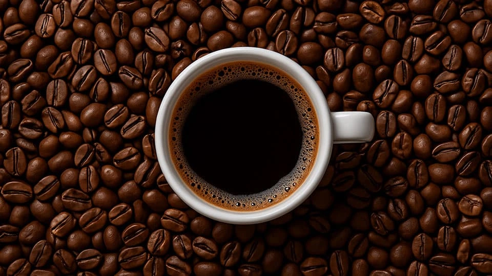 A cup of black coffee in a mug in the middle of coffee beans