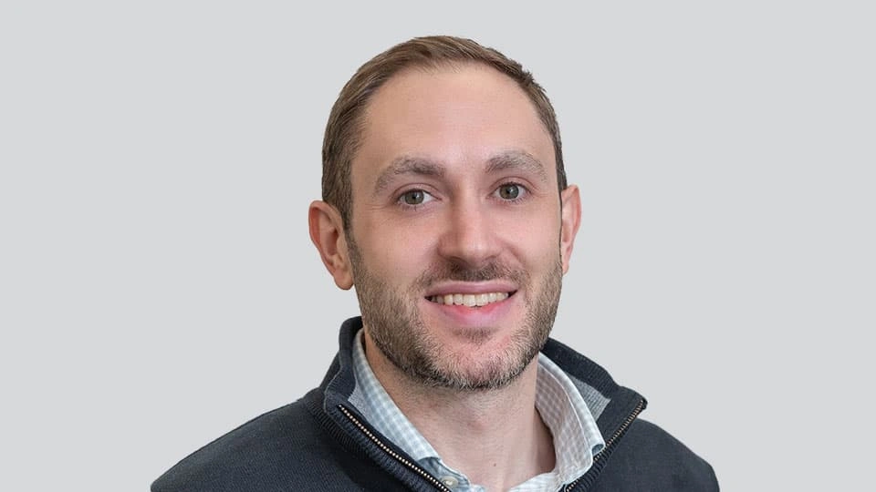 A man looking into the camera and smiling against a plain background