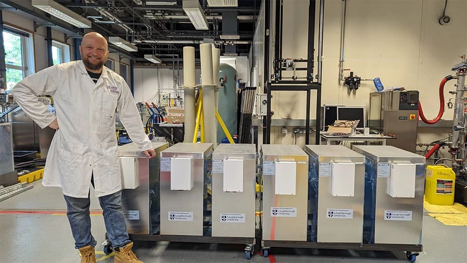 A man in a lab coat standing next to a number of cylinders in a large warehouse