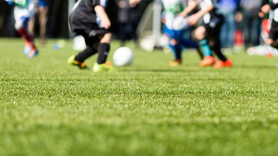 A group of blurred people playing football in the background on artificial grass