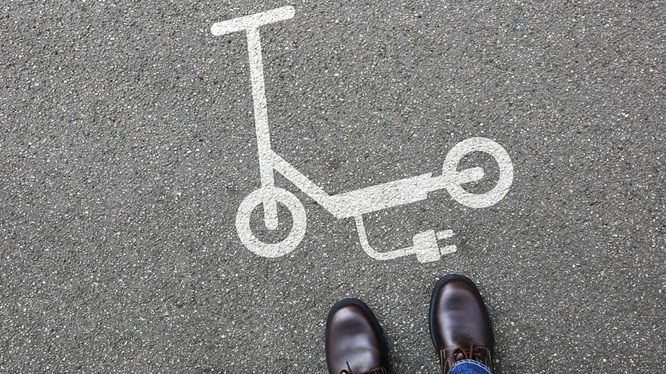 An image of an electric scooter on a pavement with a person stood next to it