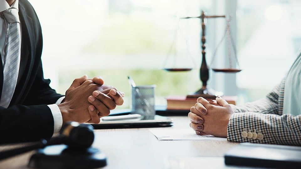 Two sets of hands clasped over a table with a legal symbol in the background