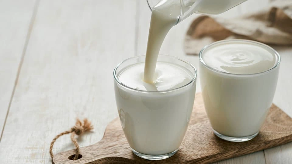 A jug of milk being poured into a glass on top of a wooden board