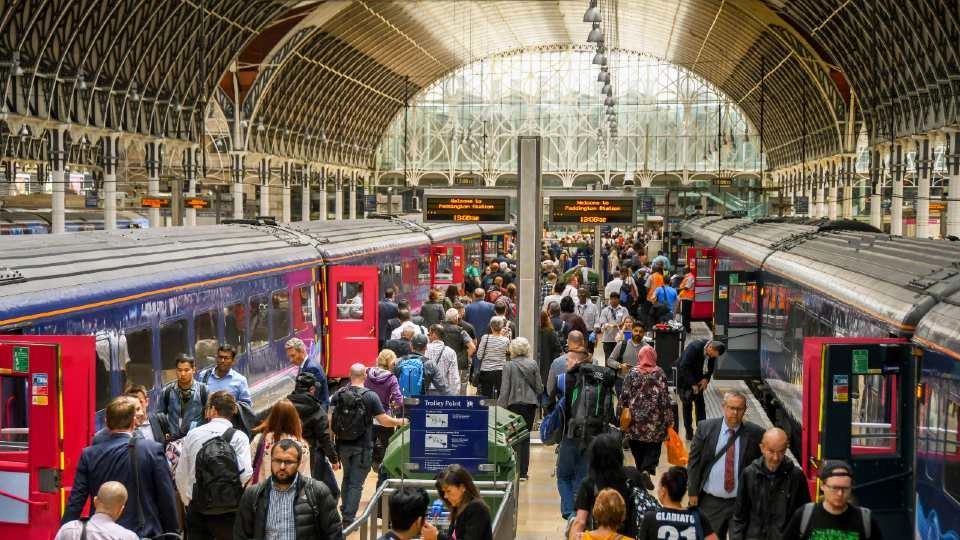 An indoor trains station with two train carriages in shot. There is a large group of people on the platform moving towards the carriages.
