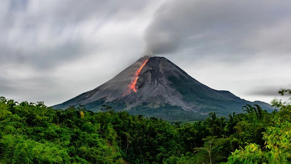 A landscape image of a volcano erupting in the distance with smoke coming out the top