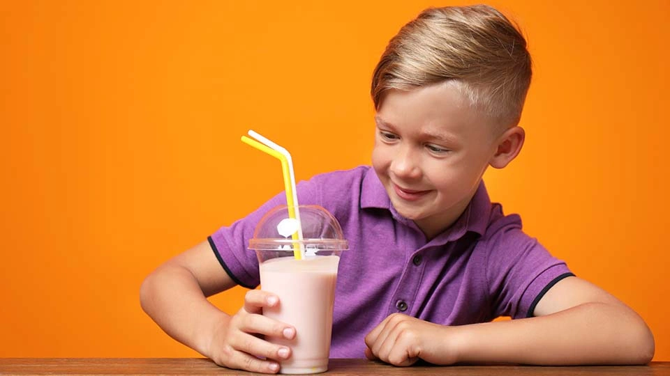 A boy looks at a glass of strawberry milkshake