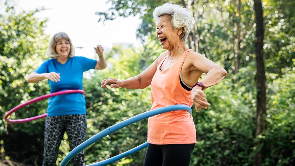 Two elderly women hula hoop outdoors