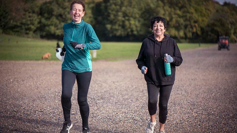 Two women jog outdoors on a gravel path